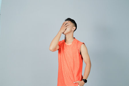 a young man wearing an orange shirt is showing a disappointed gesture, isolated on a gray backgroundの写真素材