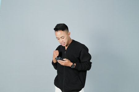 a young man wearing a black shirt is interacting with his smartphone, isolated on a gray backgroundの写真素材