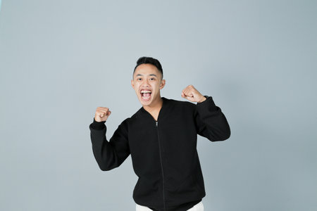 a young man wearing a black shirt is happy for an achievement, isolated on a gray backgroundの写真素材