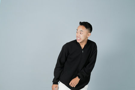 a young man wearing a black shirt is staying away from something he doesn't like, isolated on a gray backgroundの写真素材