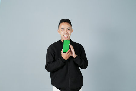 a young man wearing a black shirt is showing something on his smartphone happily, isolated on a gray backgroundの写真素材