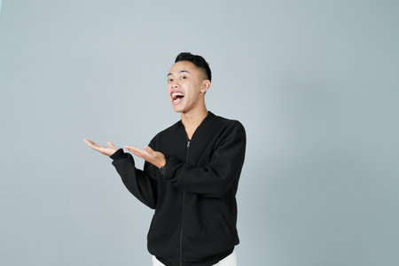 a young man wearing a black shirt is showing something happily, isolated on a gray backgroundの写真素材