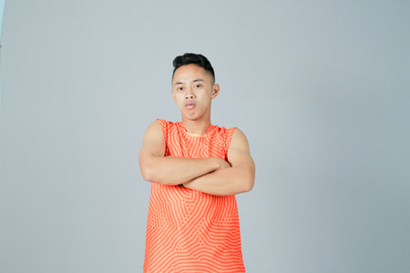 a young man wearing an orange shirt is showing a strong gesture, isolated on a gray backgroundの写真素材