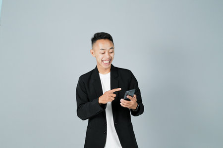 a young man wearing a black suit is interacting with his smartphone, isolated on a gray backgroundの写真素材