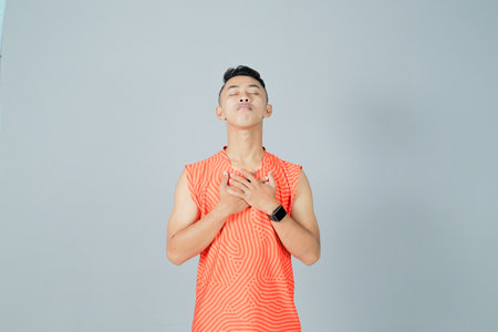 a young man wearing an orange shirt is showing a gesture of enthusiasm, isolated on a gray backgroundの写真素材