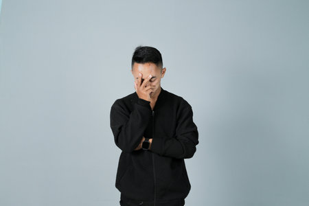 a young man wearing a black shirt is lamenting his anxiety, isolated on a gray backgroundの写真素材