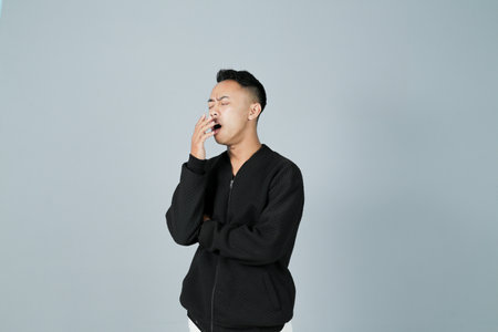 a young man wearing a black shirt is sleepy, isolated on a gray backgroundの写真素材