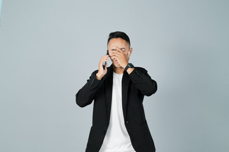 a young man wearing a black suit is stressed, isolated on a gray backgroundの写真素材