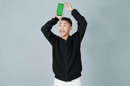 a young man wearing a black shirt is showing something on his smartphone happily, isolated on a gray backgroundの写真素材