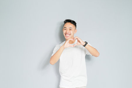 a young Asian man is smiling while showing the symbol of loveの写真素材