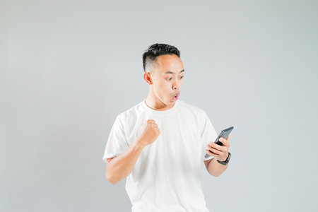 a young Asian man is excited while looking at his smartphoneの写真素材