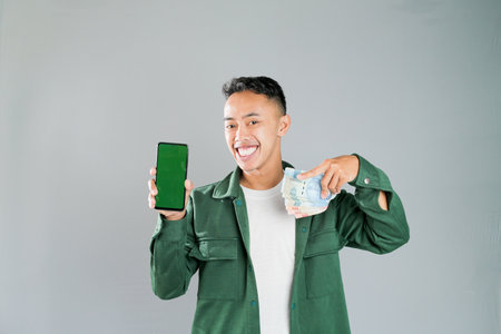a young asian man is holding a smartphone and some moneyの写真素材