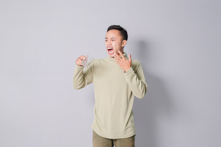 young asian man carrying a glass of drinking water, isolated on gray backgroundの写真素材