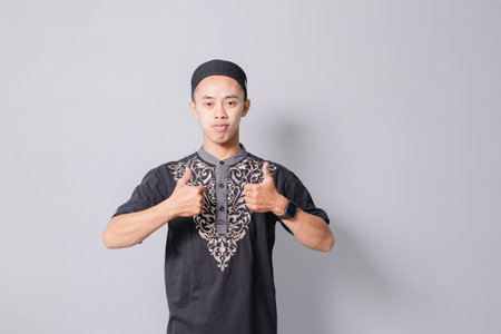 young asian muslim man giving thumbs up, isolated on gray backgroundの写真素材