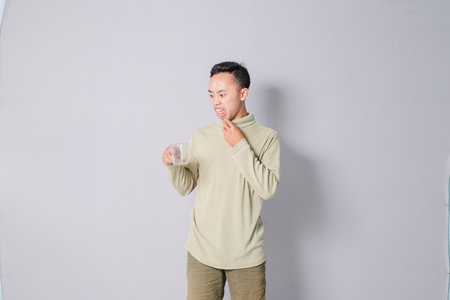 young asian man carrying a glass of drinking water, isolated on gray backgroundの写真素材
