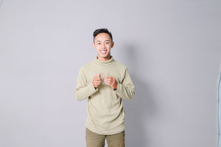 young asian man carrying a glass of drinking water, isolated on gray backgroundの写真素材