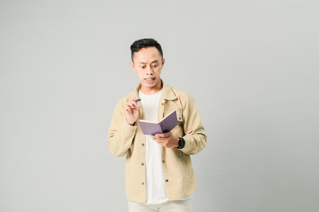 young asian man holding book and pen, isolated on gray background