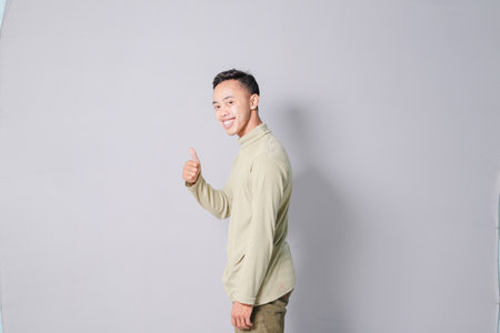 young asian man giving thumbs up, isolated on gray backgroundの写真素材