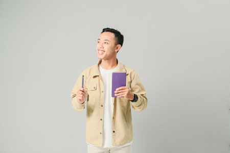young asian man holding book and pen, isolated on gray backgroundの写真素材