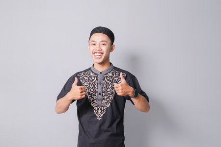 young asian muslim man giving thumbs up, isolated on gray backgroundの写真素材