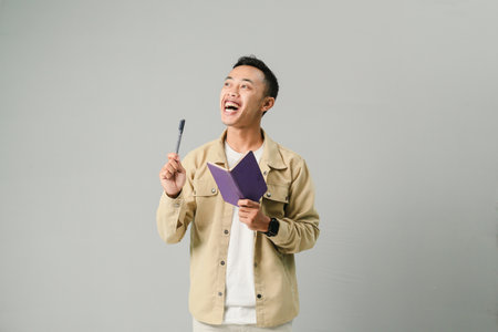 young asian man holding book and pen, isolated on gray backgroundの写真素材