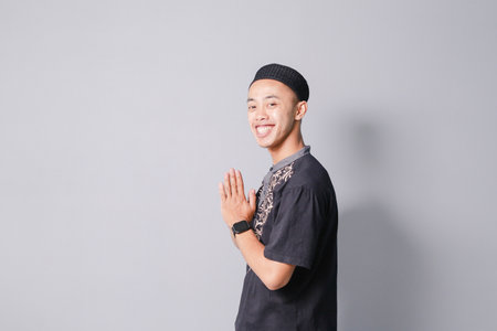 young asian muslim giving greeting, isolated on gray backgroundの写真素材