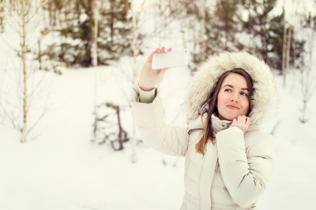 Girl taking selfie. Christmas girl outdoor self portrait. Woman in winter clothes on a snow field. Toned pictureの写真素材