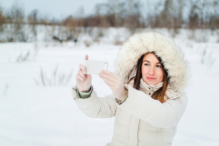 Girl taking selfie. Christmas girl outdoor self portrait. Woman in winter clothes on a snow field.の写真素材
