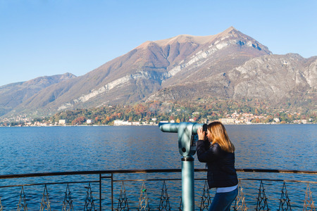 Young girl looking through a coin operated binoculars. Bellagio, Como Lake, Italy.の写真素材