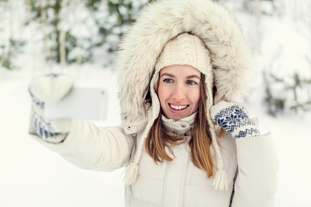 Girl taking selfie. Christmas girl outdoor self portrait. Woman in winter clothes on a snow field.の写真素材