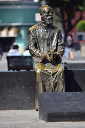 Toluca, MÃ©xico State / MÃ©xico - June 14, 2014: A statue of an old man, sitting with a book on his hands, while people can be seen chilling around downtown.のeditorial素材