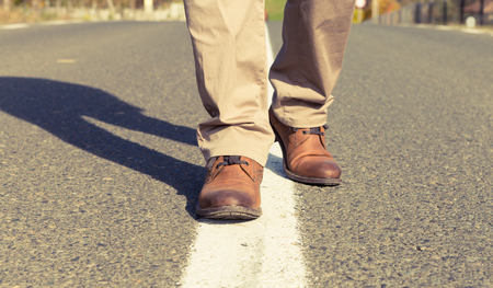 Male feet walking and wearing atutumn real leather shoes. Center of the asphalt roadの写真素材