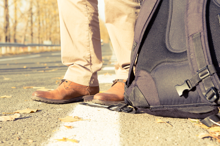 Feet and backpack of a male traveler or hitchhiker, wearing brown genuine autumn leather shoes as fall fashion conceptの写真素材