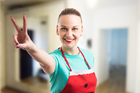 Happy smiling housewife showing peace vistory gesture indoors as clean house conceptの写真素材