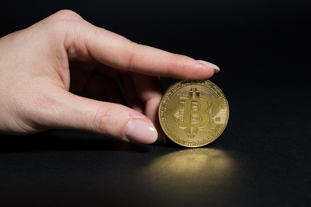 Woman hand holding a golden bitcoin on dark backgroundの写真素材