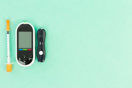 Glucometer and insulin syringe on green background as sugar level or glucose measure concept with copyspaceの写真素材