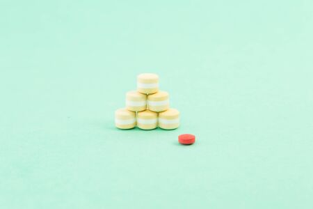 Pile of pills or tablets and a red one as out of pattern concept on medical green background