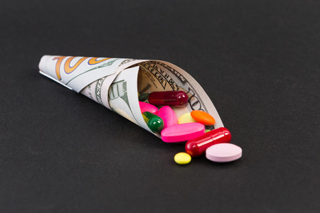 Pills and capsules wrapped in one hundred dollar bill isolated on dark black background
