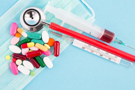 General medical concept with syringe stethoscope thermometer and pills on surgical maskの写真素材