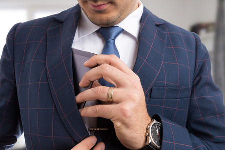 Elegant male placing expensive smartphone in suit jacket pocket as luxury conceptの写真素材