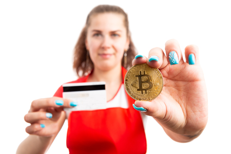 Young woman supermarket or hypermarket worker holding bitcoin symbol and credit card as payment choice concept isolated on white backgroundの写真素材