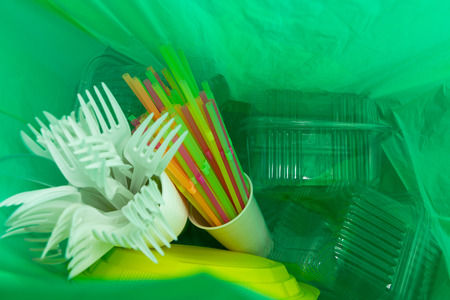 Inside of green plastic bag with single use cutlery plates straws cup and package boxes as ecology...