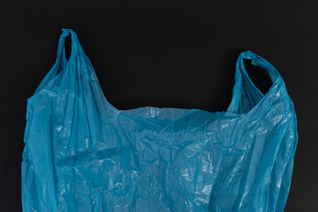 Used crumpled single use blue plastic bag with handles as waste pollution environment ecology concept isolated on black backgroundの写真素材