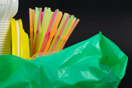 Closeup of colorful plastic waste in a green garbage bag as recyclable single use cutlery pollution junk concept isolated on black backgroundの写真素材