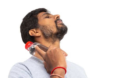 Artistic picture isolated on white background of indian man touching neck with cold plastic water bottle as hot summer conceptの写真素材
