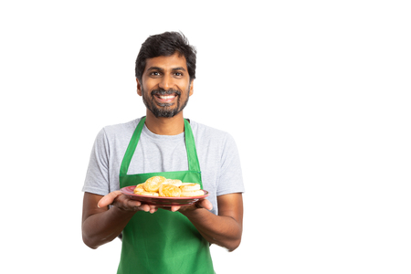 Cheerful indian man employee at supermarket or hypermarket presenting dish with donuts with happy expression isolarted on whiteの写真素材