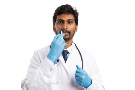 Indian doctor man using nasal spray as flu or allergy concept isolated on white studio backgroundの写真素材