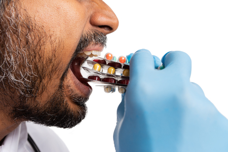 Close-up of indian male doctor or medic eating pill blisters isolated on white backgroundの写真素材