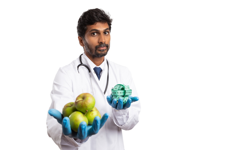 Indian male dietician or medic holding green apples in one hand and measuring tape in the other as healthy lifestyle concept isolated on whiteの写真素材