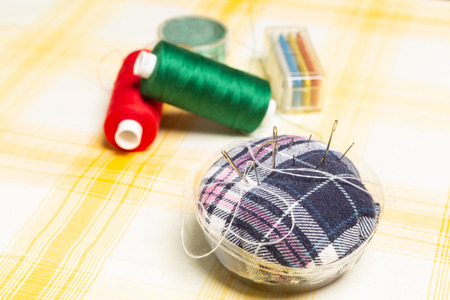 Fabric needle holder selective focus with red and green colourful thread spools